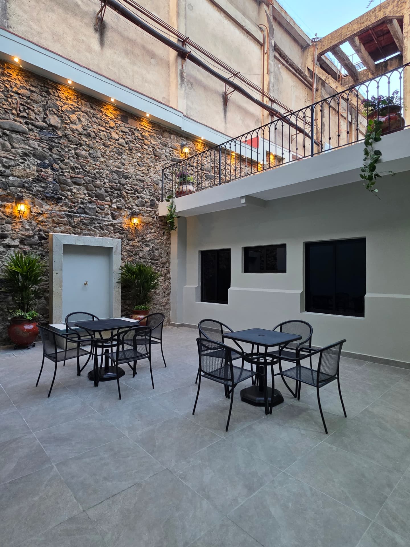 Patio interior con mesas, sillas y muro de piedra original